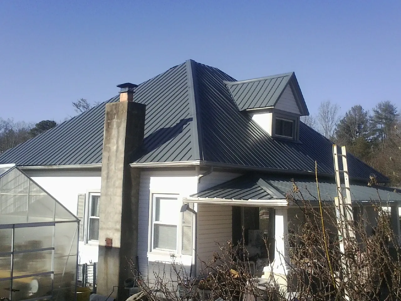 Dark blue standing seam metal roof on a white farmhouse with dormer — Slate & Tile Roof Repair by Roofing Brothers in Poolville