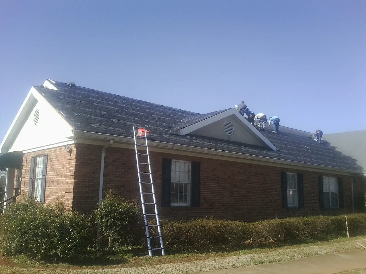 Crew tearing shingles off a brick ranch roof with a ladder set — Emergency Roof Repair work by our crew in Poolville