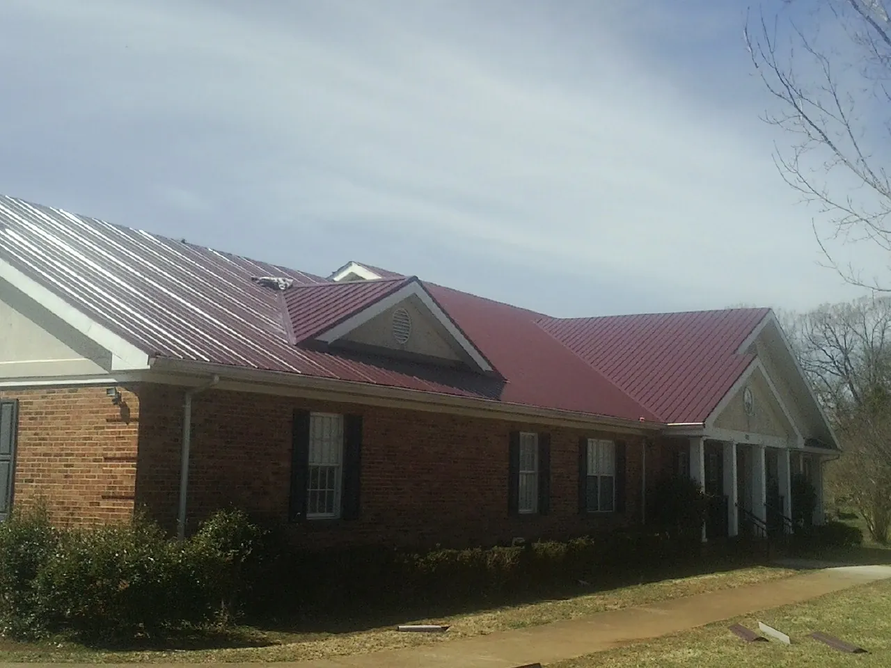 Red metal roof with gabled entries on a long brick building, from a Hail Damage Roof Repair job in Poolville