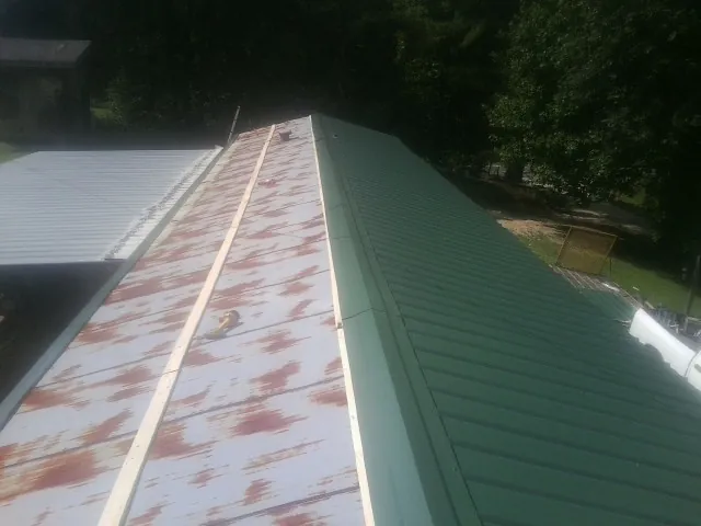 Old rusted panels beside newly installed green metal roofing — Wind Damage Roof Repair by Roofing Brothers in Poolville
