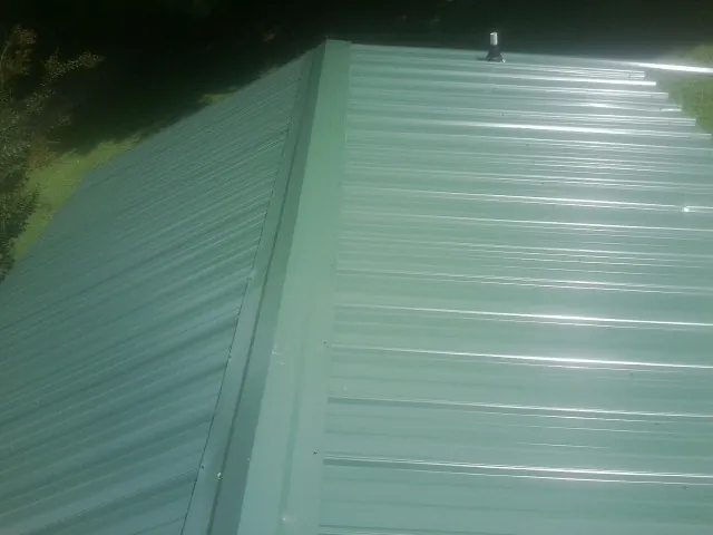 New green metal panels meeting at the ridge of a roof — Flat Roof Repair work by our crew in Poolville