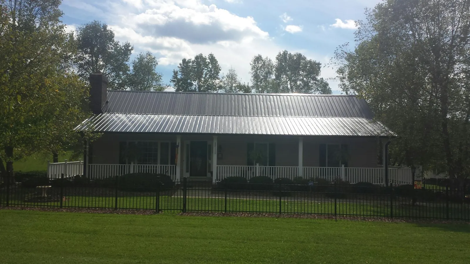 Gray metal roof on a brick ranch with a full width front porch — Gutter Guard Installation work by our crew in Poolville